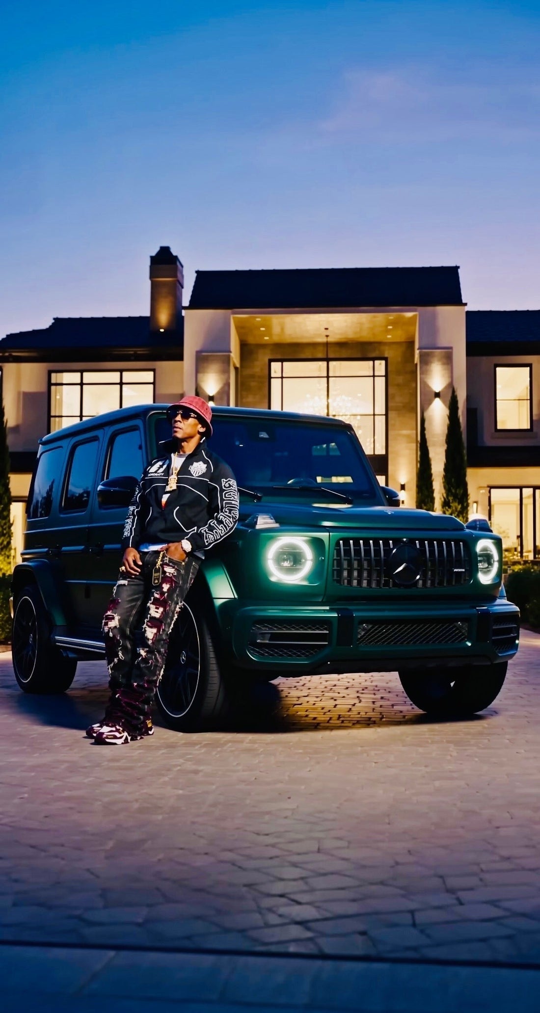 Honorable Society founder leaning on a green Mercedes-AMG G-Wagon outside a lit estate at blue hour
